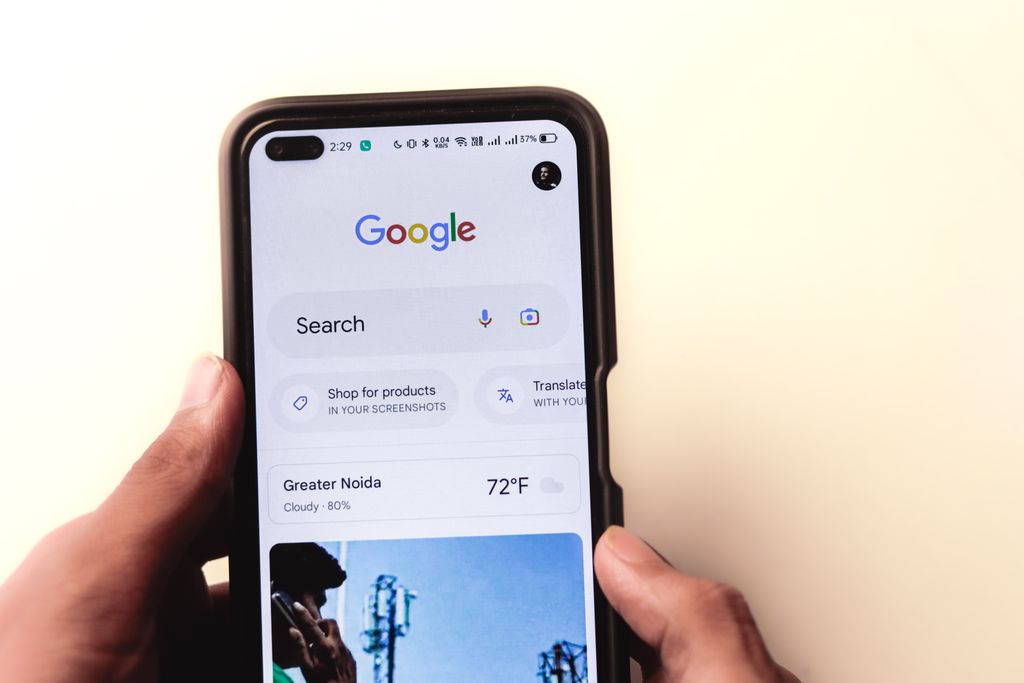 A close-up of a hand holding a smartphone with Google search displayed on the screen.