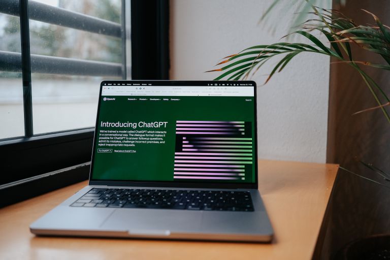 Best AI Productivity Tools A laptop displaying ChatGPT on a desk by a window, featuring a modern home office setup.
