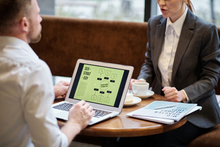 How to Become a Successful SEO A man and woman engaged in a business meeting discussing SEO strategy in a cozy cafe setting.