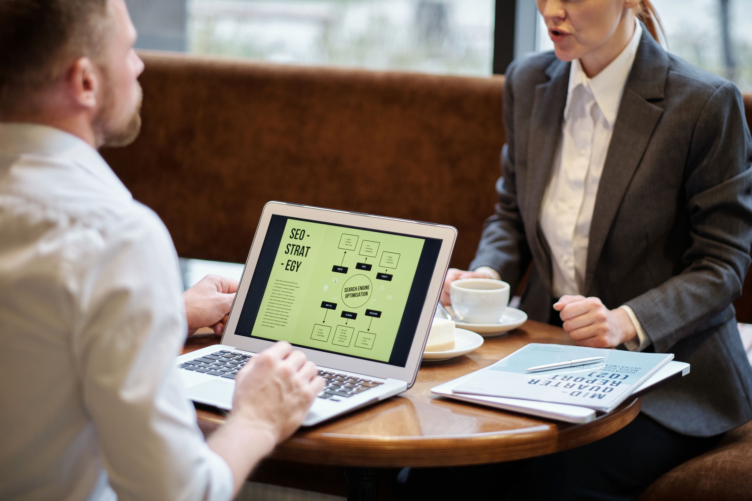 How to Become a Successful SEO A man and woman engaged in a business meeting discussing SEO strategy in a cozy cafe setting.