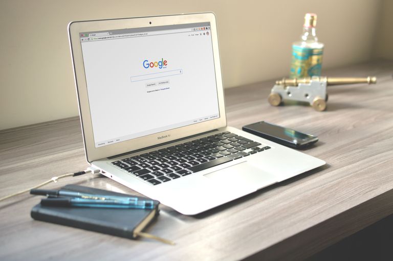 Best Free Tech Tools Every Website Owner Should Know in 2026 A neat workspace featuring a laptop displaying Google search, a smartphone, and a notebook on a wooden desk.