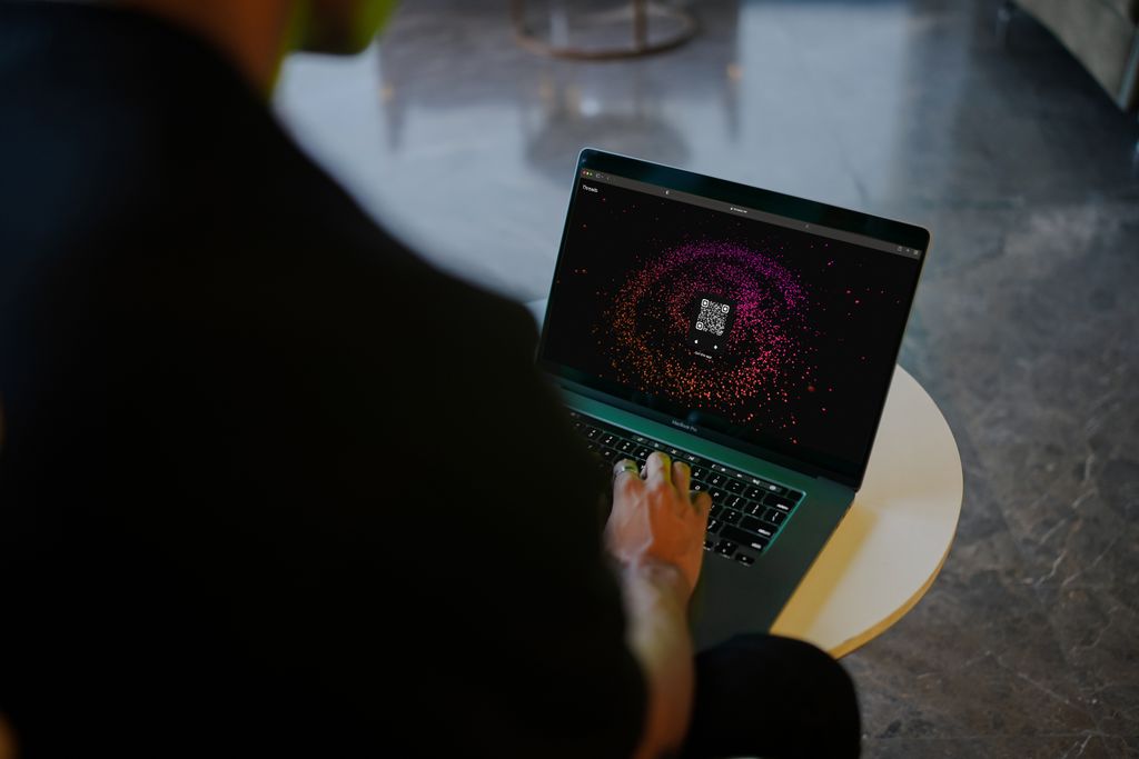 A person interacts with a colorful QR code display on a laptop in a modern indoor setting.