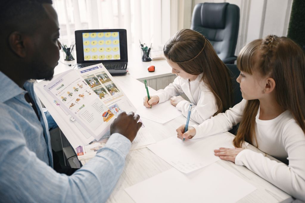  Technology  A teacher instructing two young students in a classroom environment.