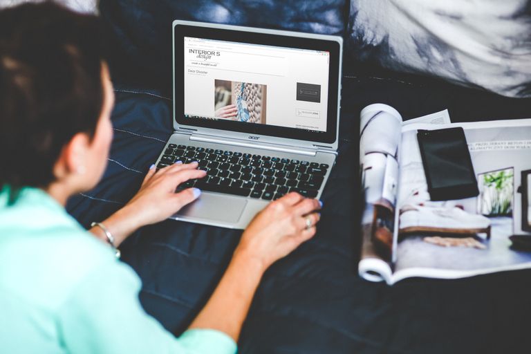 Article Upload Account A woman on a bed browsing and blogging with a laptop and a magazine nearby.