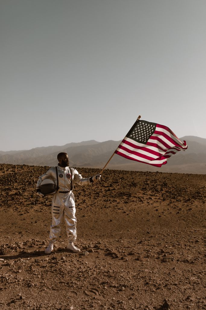 Astronaut proudly holds American flag on a barren Mars-like landscape, symbolizing exploration.