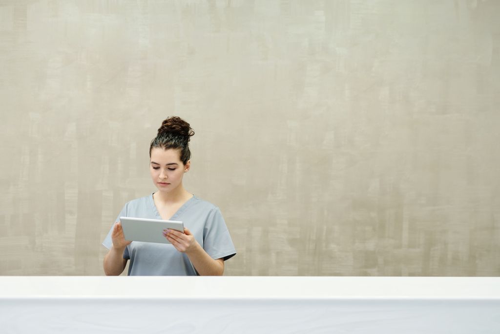 Caucasian woman in uniform using a tablet at a modern reception desk.