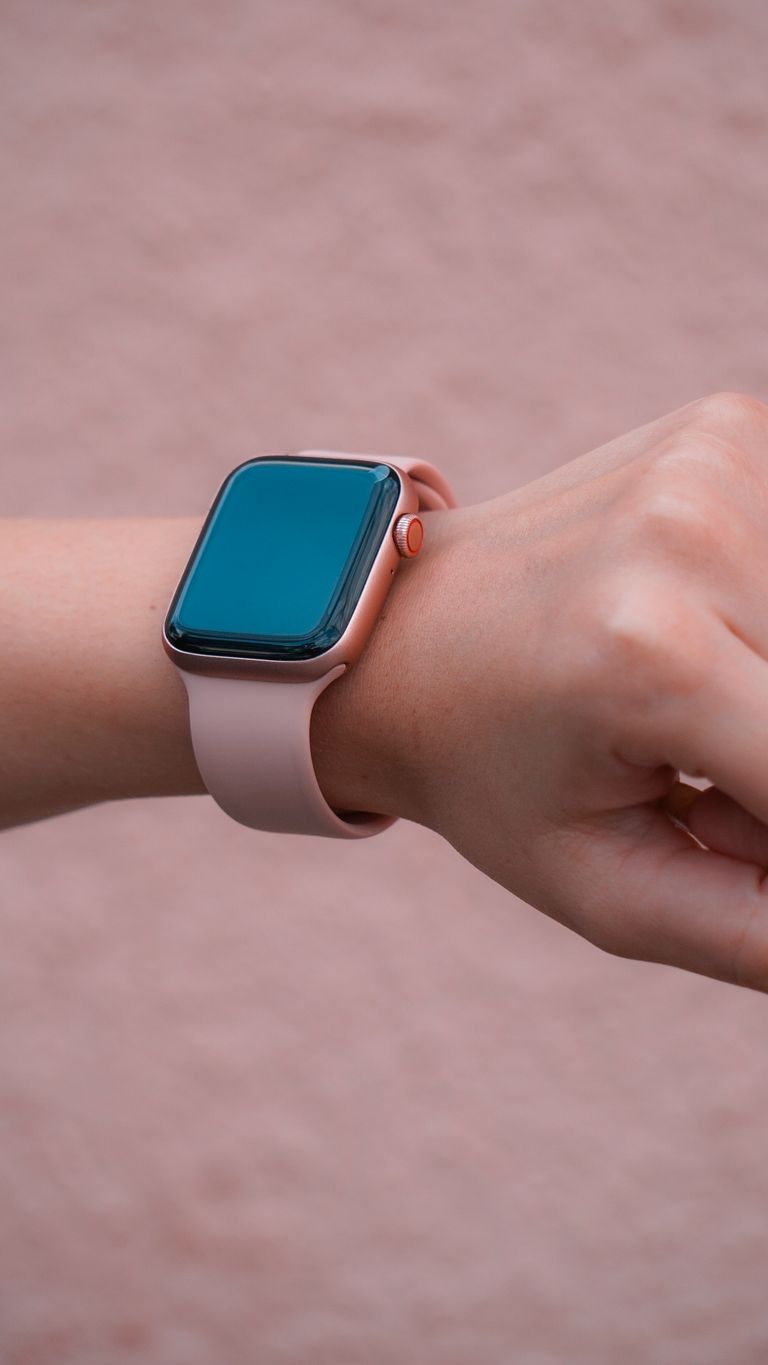 Close-up of a pink smartwatch on a person's wrist against a matching pink textured background.