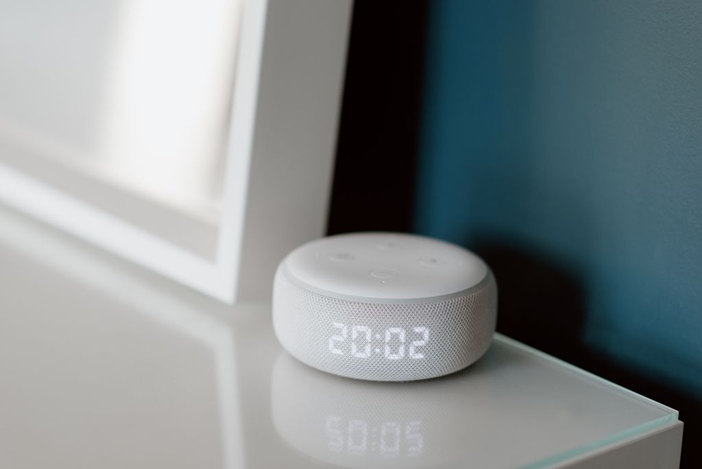 Close-up of a smart speaker with an illuminated 20:02 LED clock display on a desk.