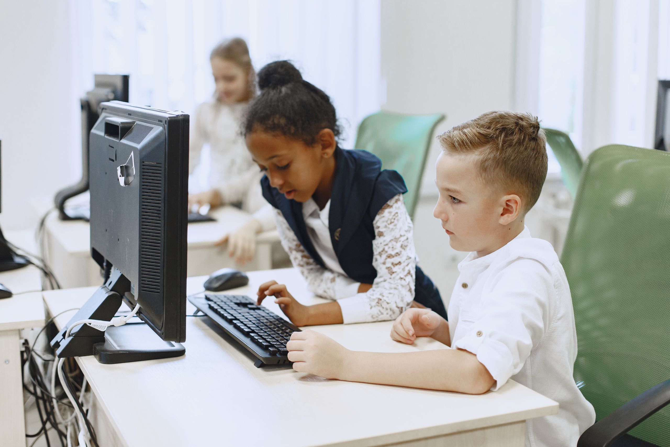 Diverse children working together on computers in a modern school setting.