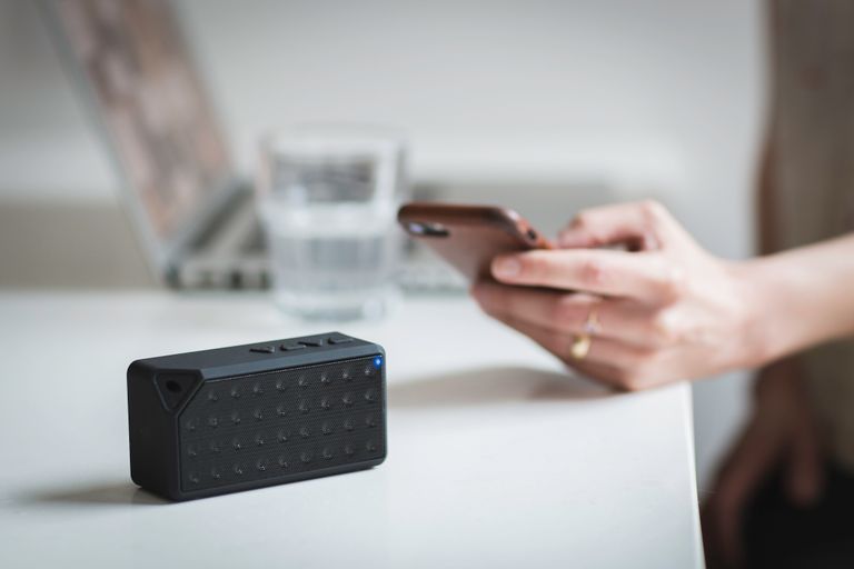 Person connecting a smartphone to a wireless speaker indoors, foreground focus.