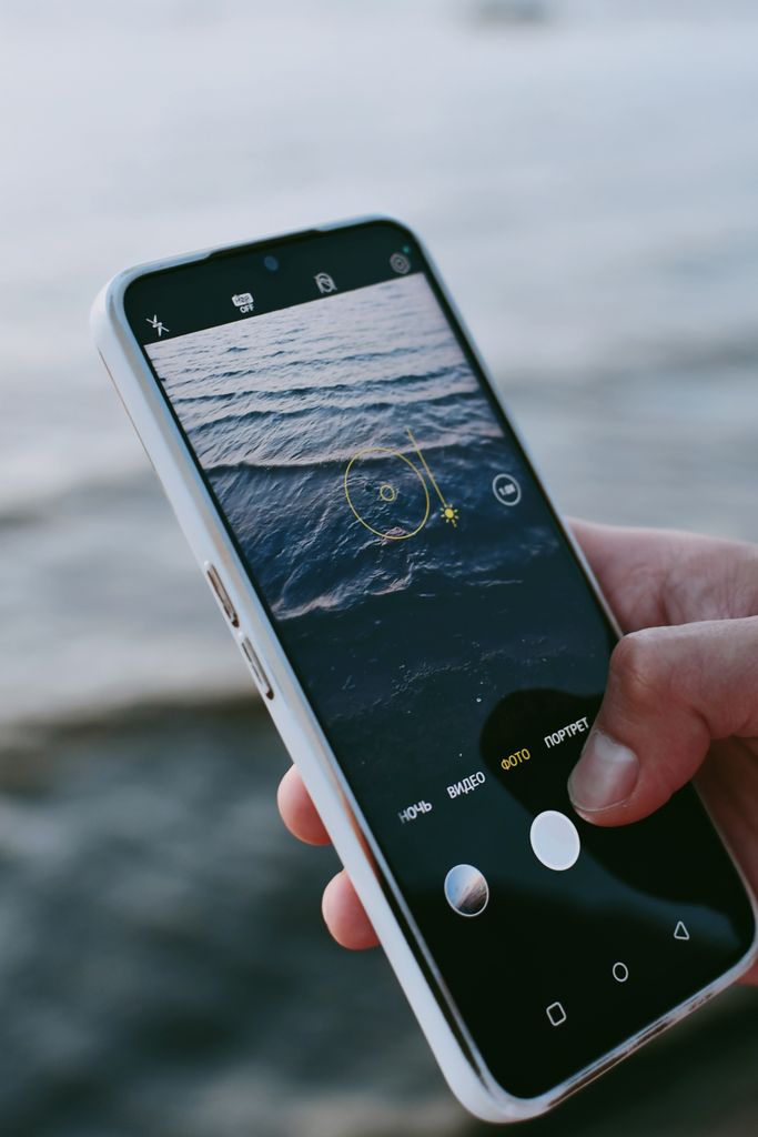 Person using smartphone to photograph waves on the beach.