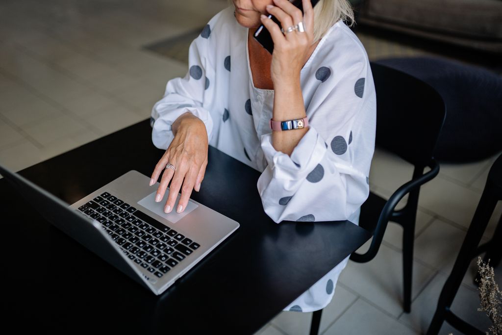 Professional woman multitasking with laptop and phone in modern setting.