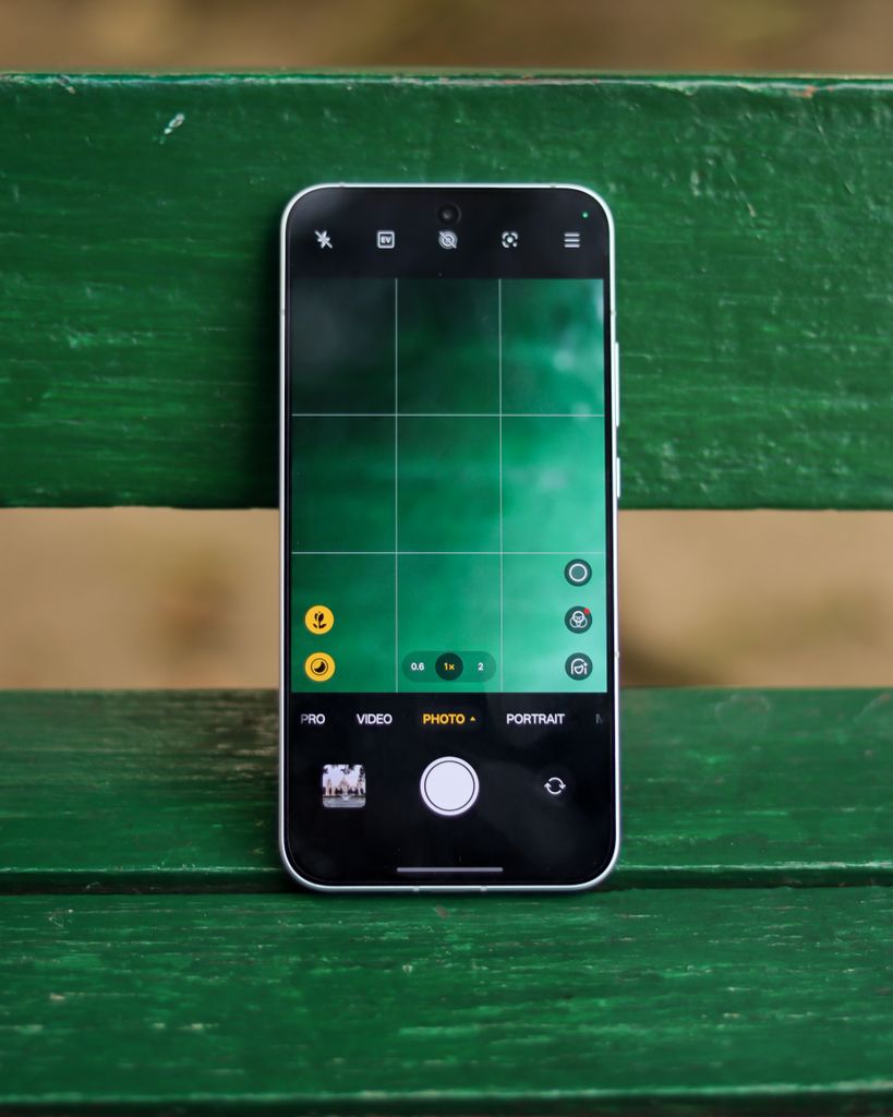 Smartphone displaying camera interface placed on a vibrant green wooden bench outdoors.