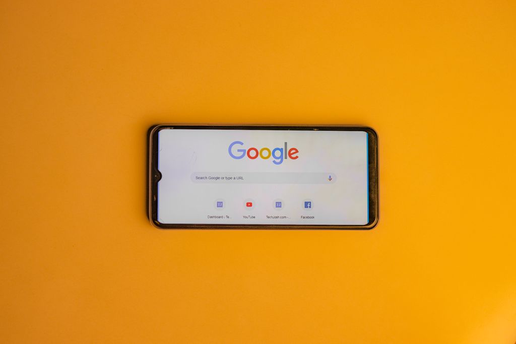 Smartphone displaying Google search page on a vibrant yellow background.
