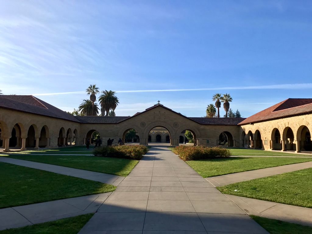 Sunny day at Stanford University's historic quad, showcasing iconic arches and palm trees.