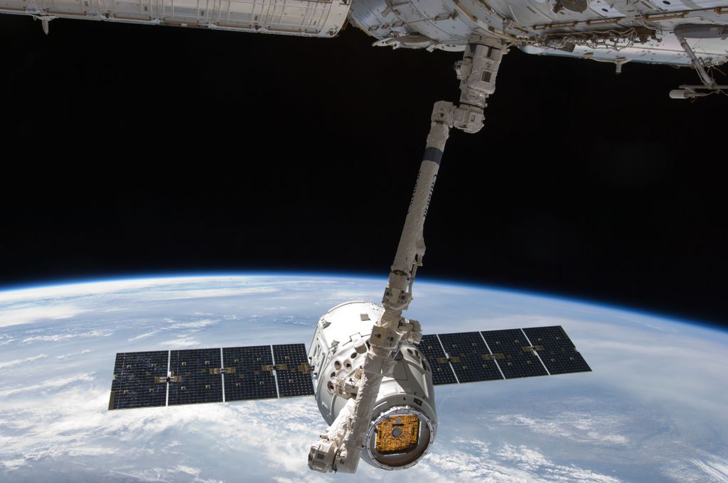 View of a spacecraft docked at the ISS above Earth with visible solar panels.